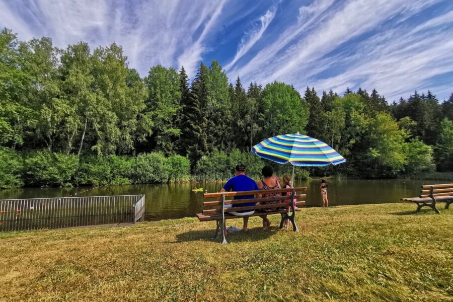 Badeteich mit Familie auf einer Bank mit Sonnenschirm