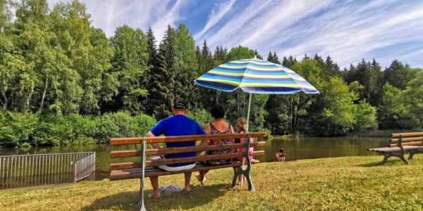 Badeteich mit Familie auf einer Bank mit Sonnenschirm
